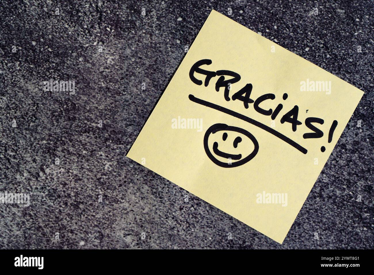 Thank you in spanish written on a post-it or note on table. Stock Photo