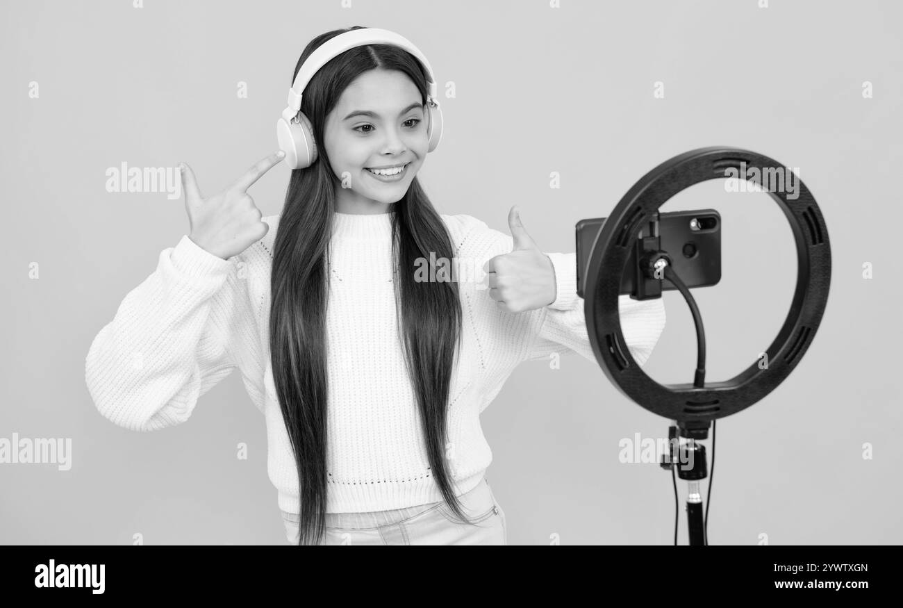 Teen girl speaking in front of camera for vlog isolated on yellow background. Teenager working as blogger, recording video blog. Stock Photo