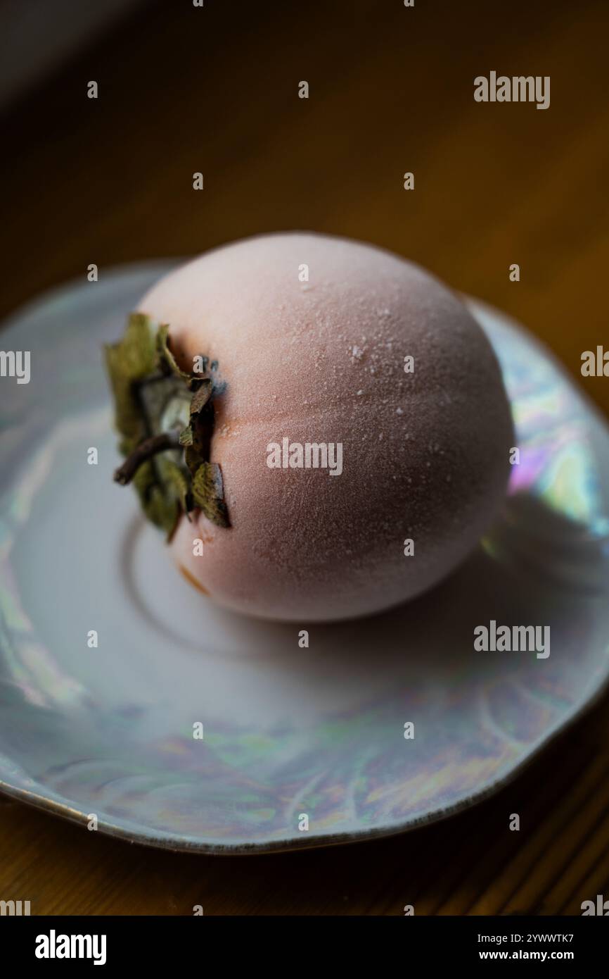 Frozen persimmon on a saucer. Persimmon covered with frost Stock Photo