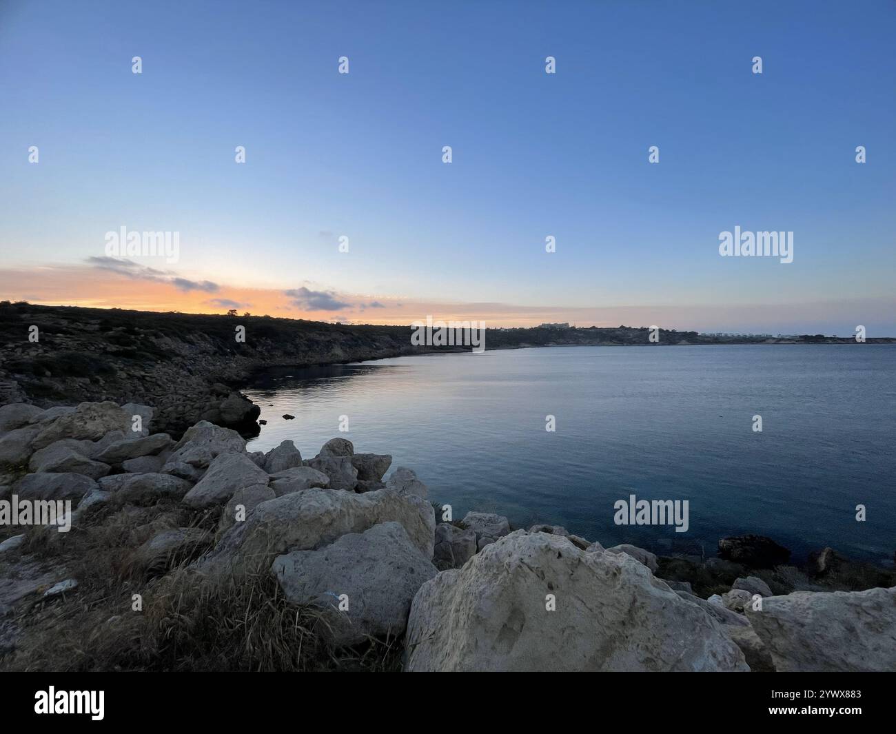 Rocky Coastal Landscape with Calm Sea Waters and a Vibrant Sunset Horizon Under a Clear Evening Sky Cyprus Ayia Napa - Smartphone Captured Stock Image