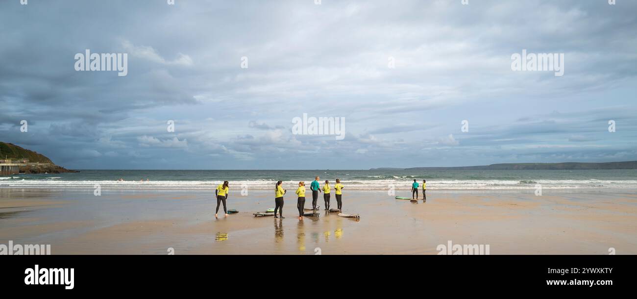 A panoramic image of a surfing instructor from the Escape Surf School with his surfing novices learners at the start of a surfing lesson on Towan Beac Stock Photo