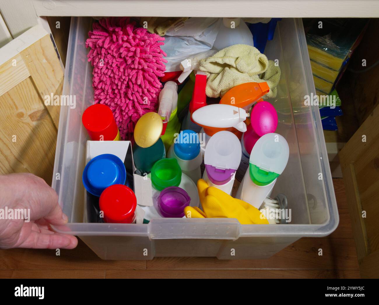 A hand holding a box or crate, containing household domestic cleaning materials, which has been pulled out from a cupboard under a kitchen sink. Stock Photo