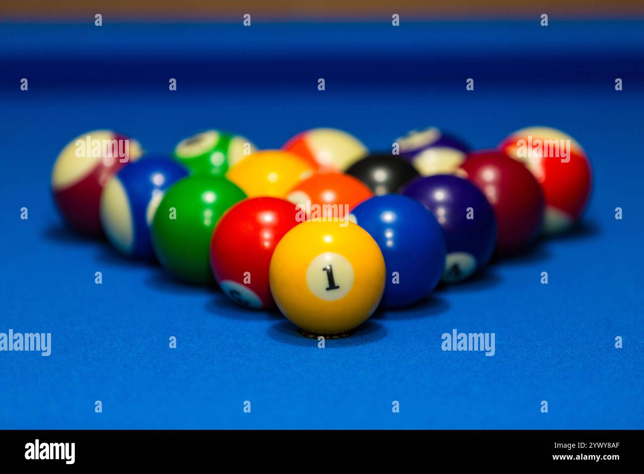 Billiard balls on a blue table. The image showcases a set of glossy billiard balls meticulously arranged in a triangular rack on a pristine blue felt. Stock Photo