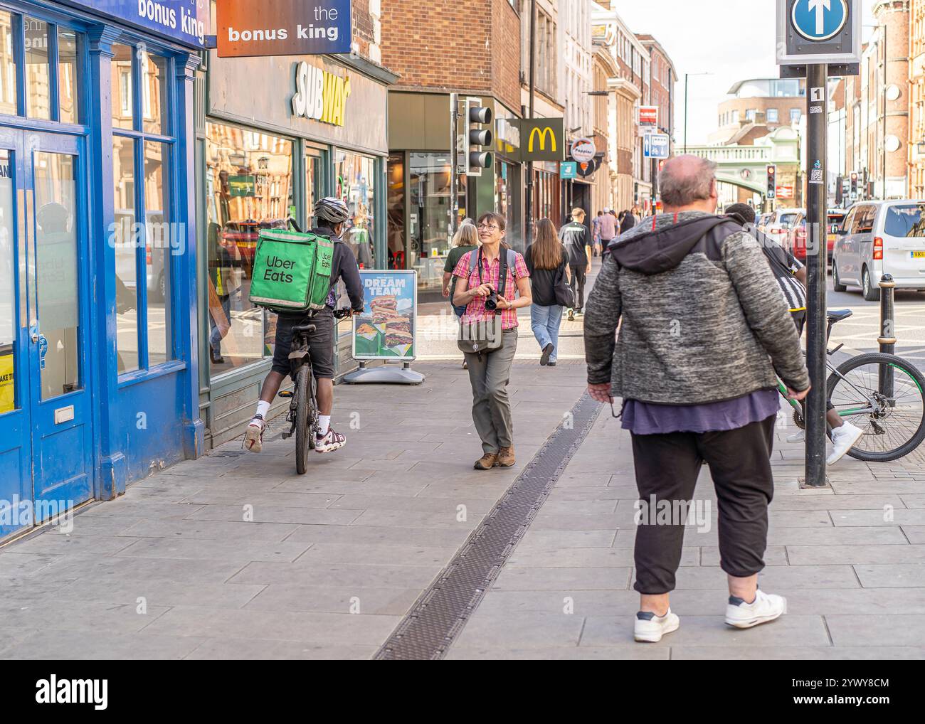 Uber Eats cyclist, with delivery box, on a busy high street riding a bike through a UK city centre. Stock Photo