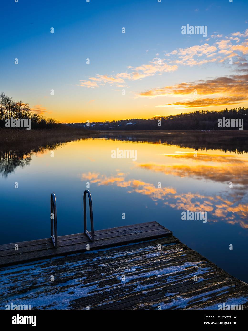 A tranquil lake is illuminated by a vibrant sunset, casting colorful ...
