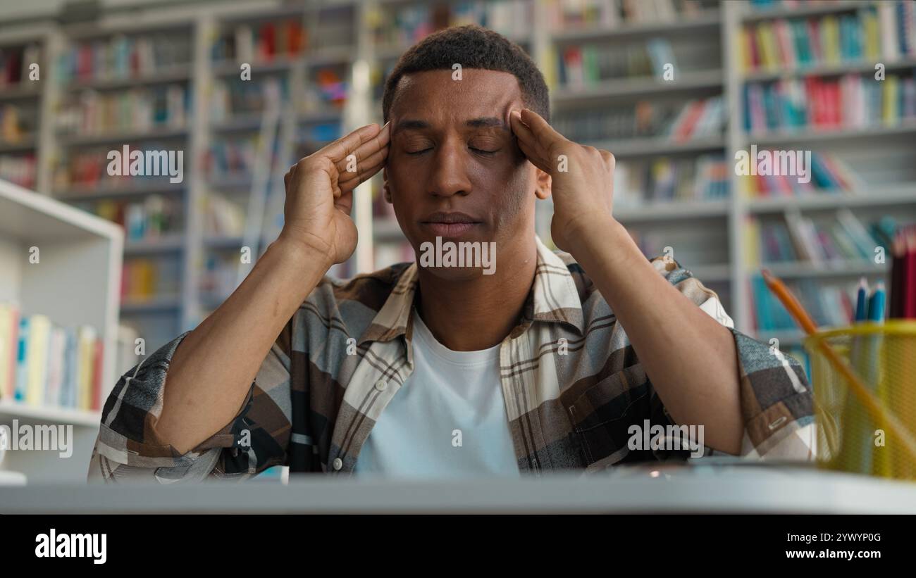 African American man guy male student massage temples headache exam tired library high school university touching head migraine eyes closed study Stock Photo