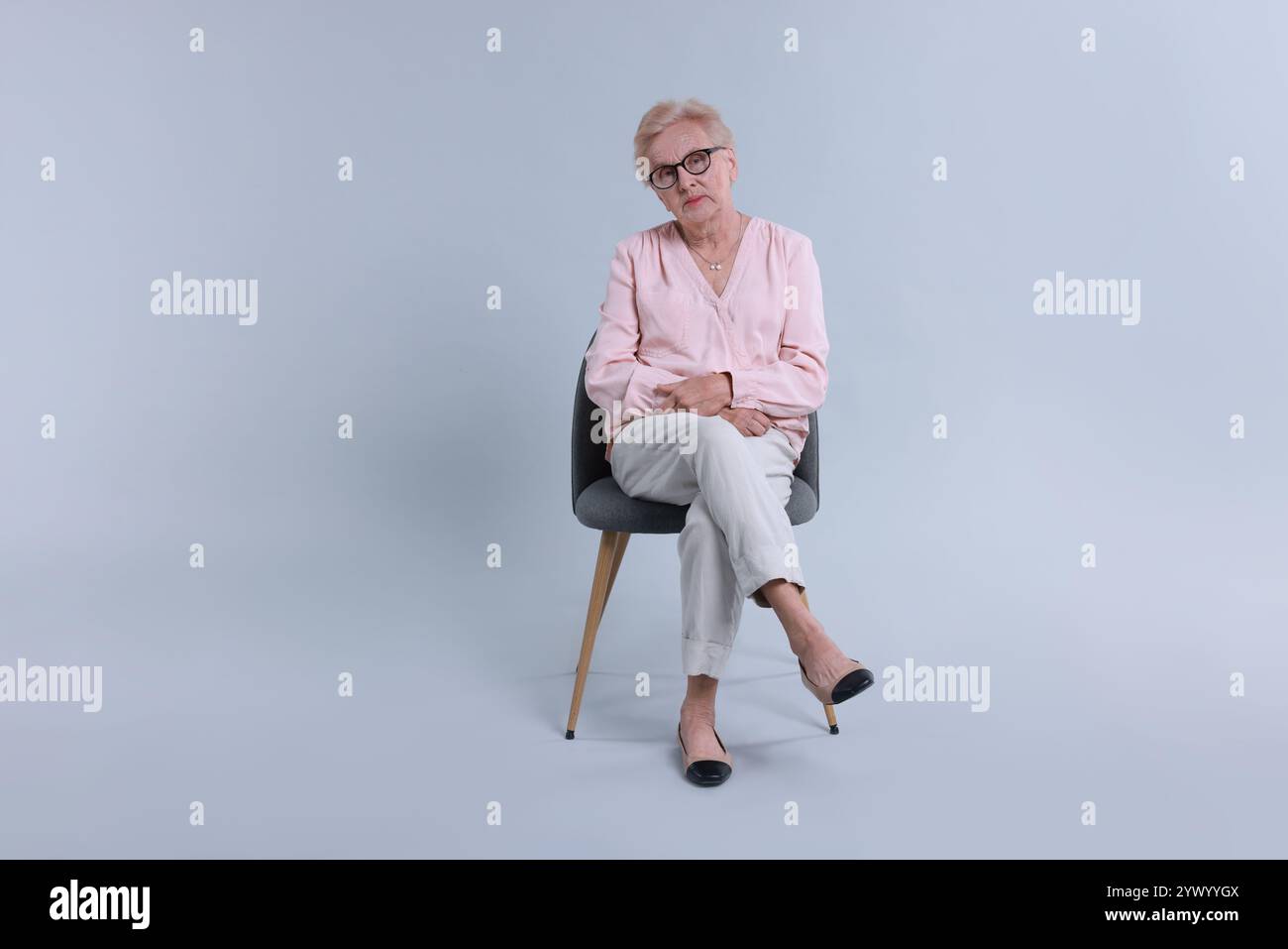 Senior woman on chair against light background Stock Photo - Alamy