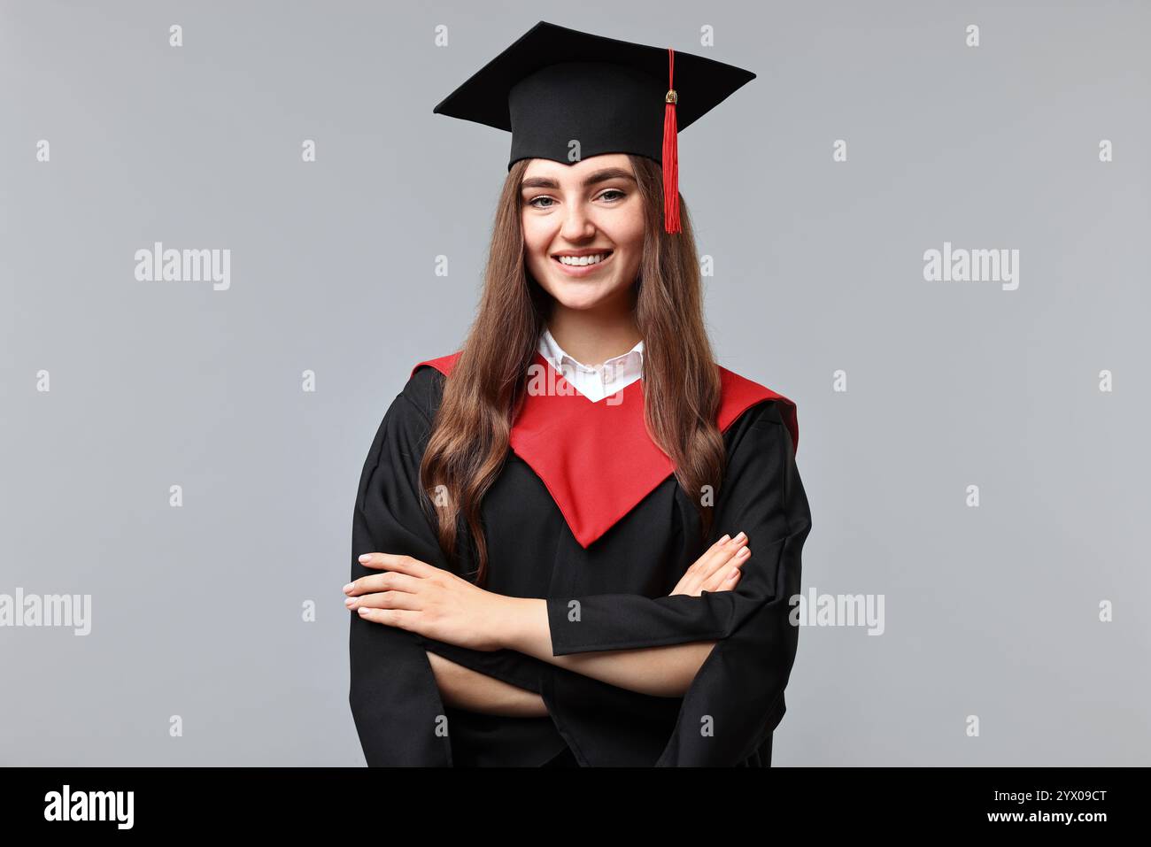 Happy student with crossed arms after graduation on grey background ...