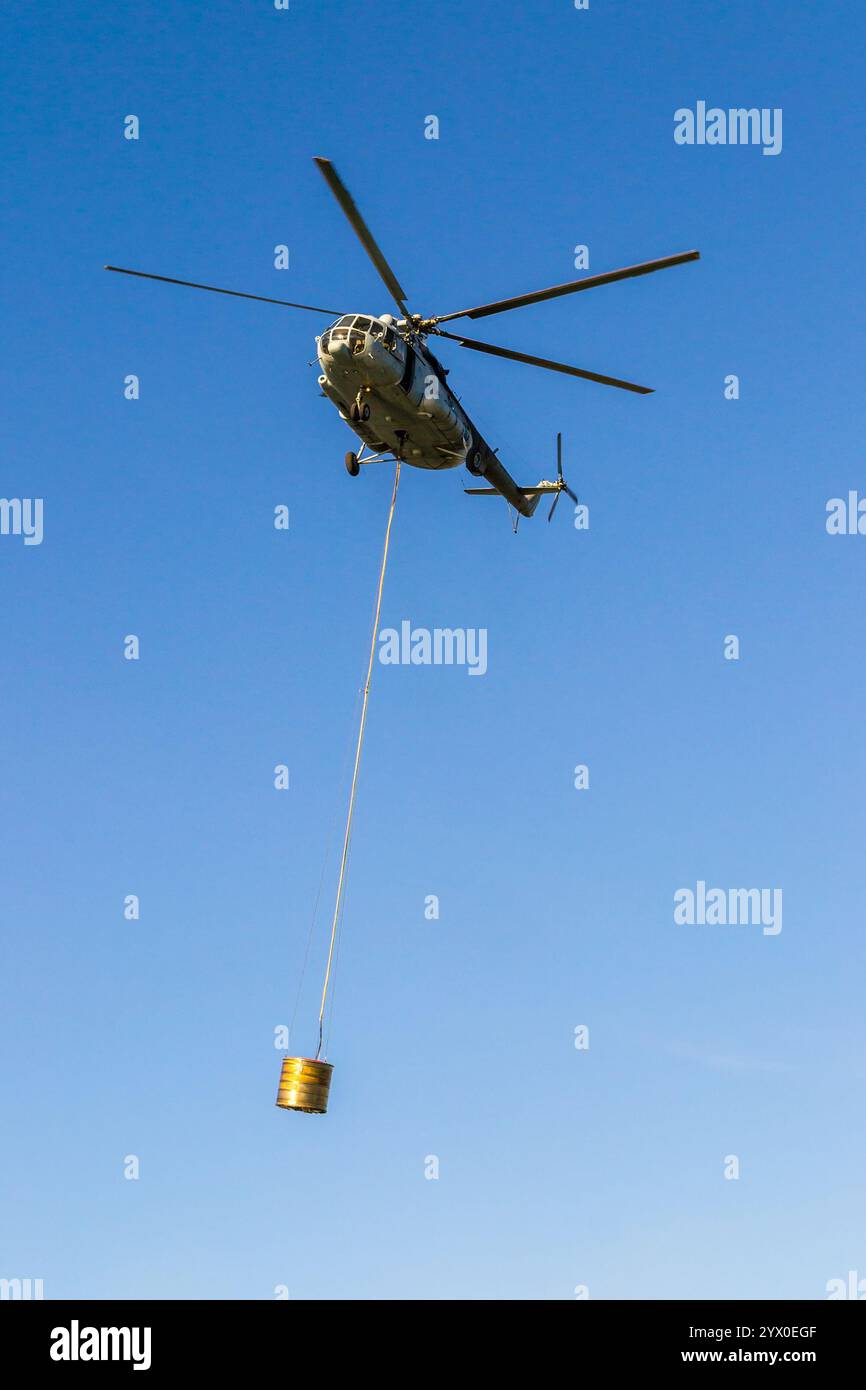 Helicopter in action carrying the water bucket. Shot from the ground. Stock Photo