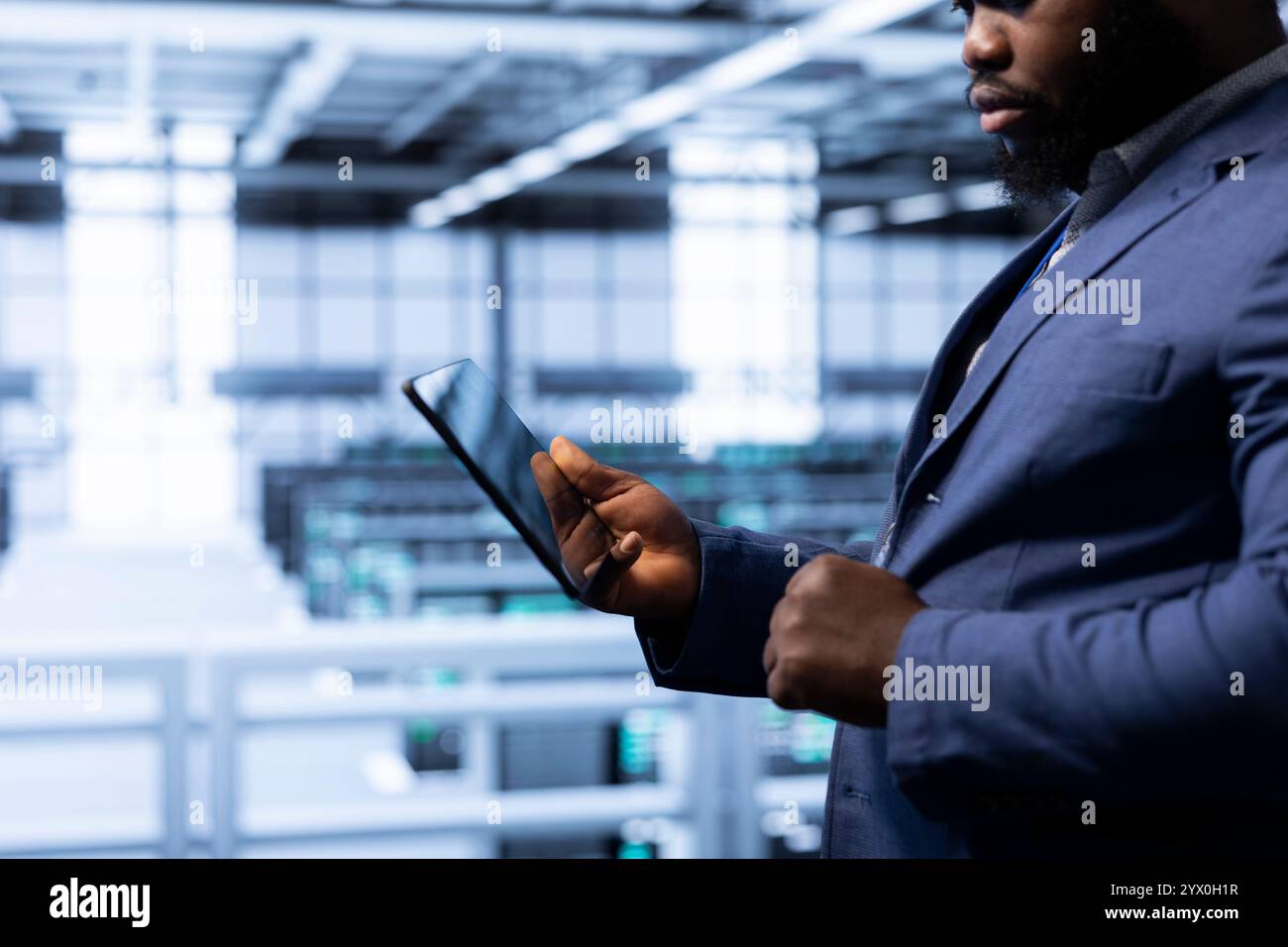 Data researcher using tablet in high tech data center, ensuring cybersecurity and efficient network management. Employee in server hub optimizing data center gear with device Stock Photo