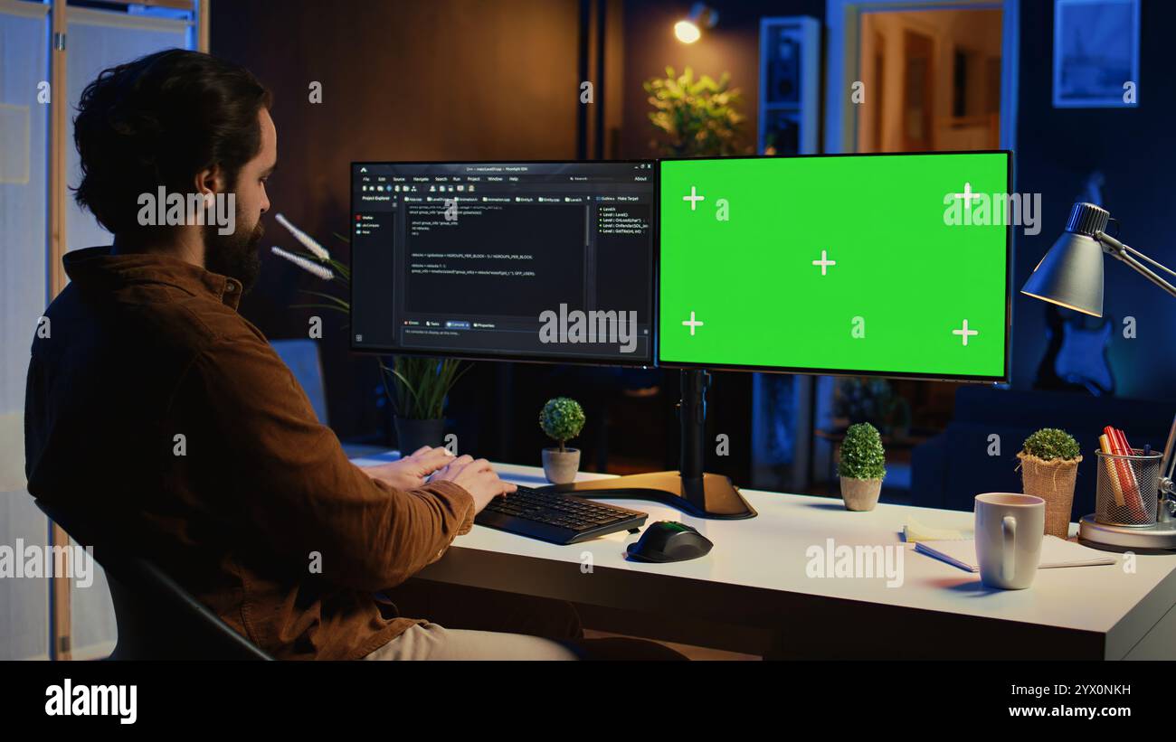 Programmer typing complex code on green screen computer in neon lit home office, developing software application. Teleworking IT specialist doing remote project tasks on mockup PC monitor, camera B Stock Photo