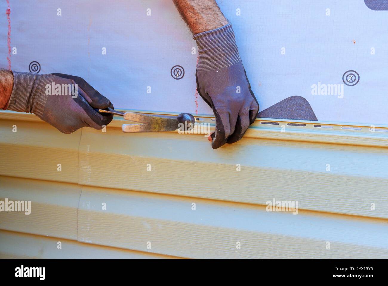 Worker carefully installs vinyl siding on house, ensuring level alignment while using hammer tools. Stock Photo