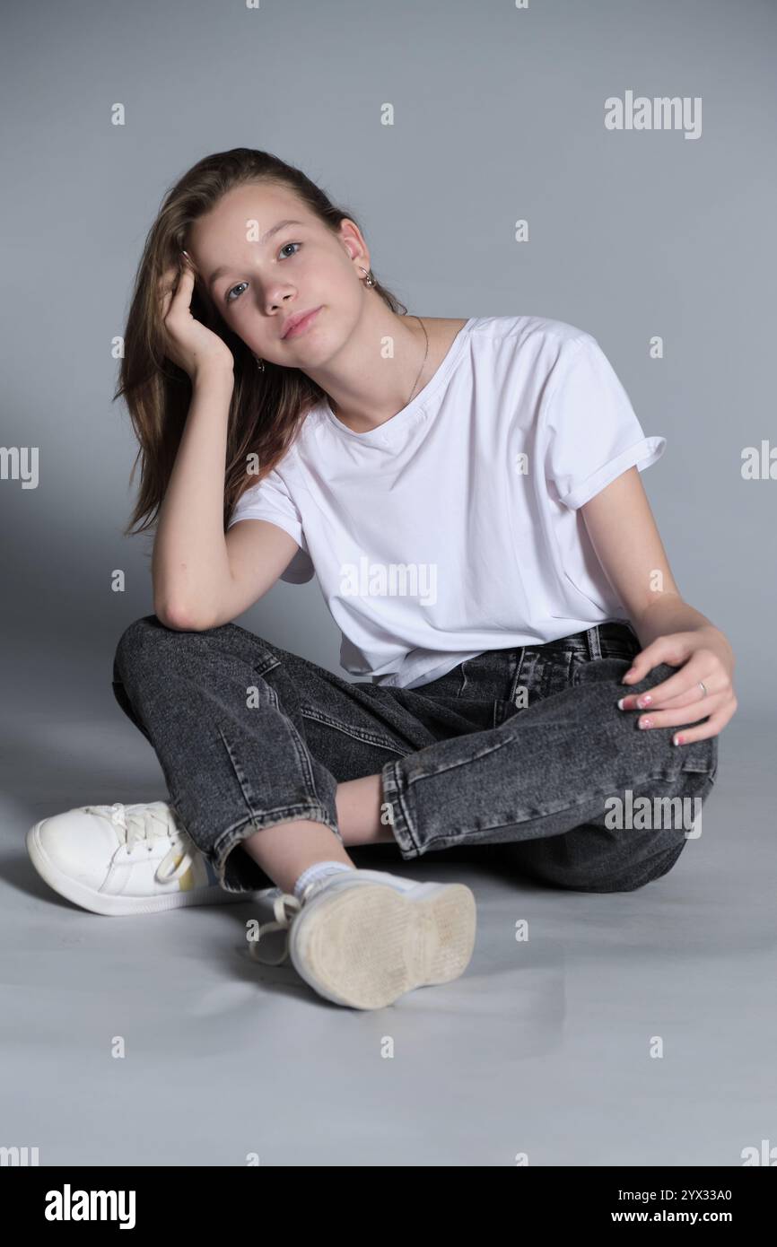 A teenage girl sits relaxed in casual clothing, resting her head on her ...