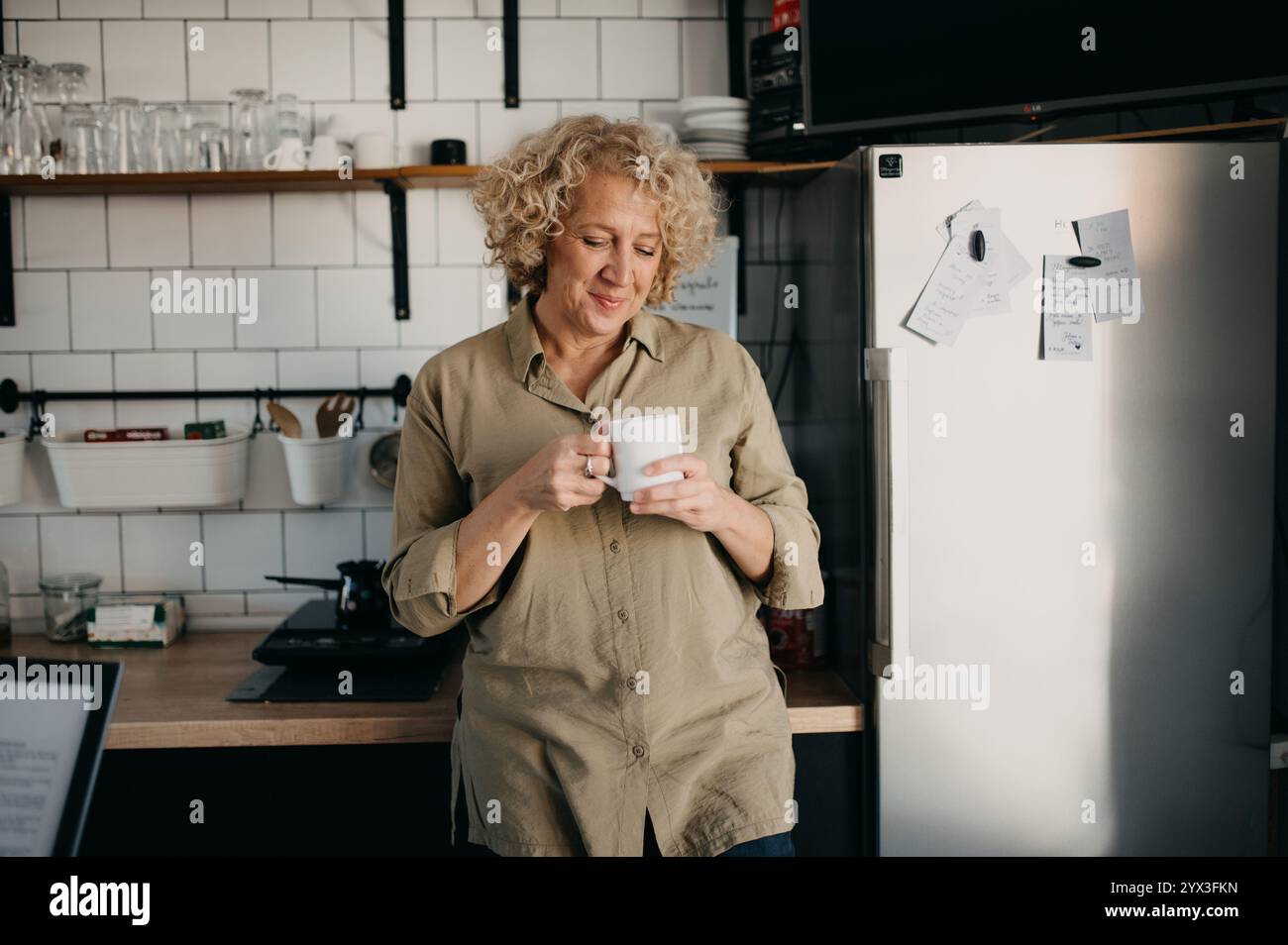 Happy middle-aged woman drinking coffee in the kitchen. Stock Photo