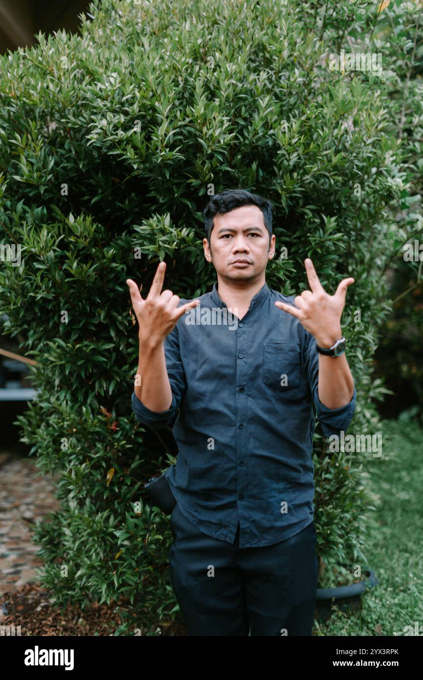 A Southeast Asian man making a metal sign with his fingers, expressing confidence and attitude. Perfect for music, lifestyle, or cultural projects hig Stock Photo