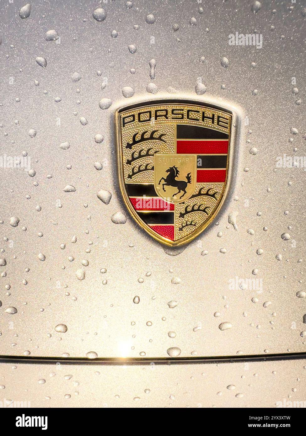 Close-up of a logo on a Porsche car hood with water droplets - Smartphone Captured Stock Image