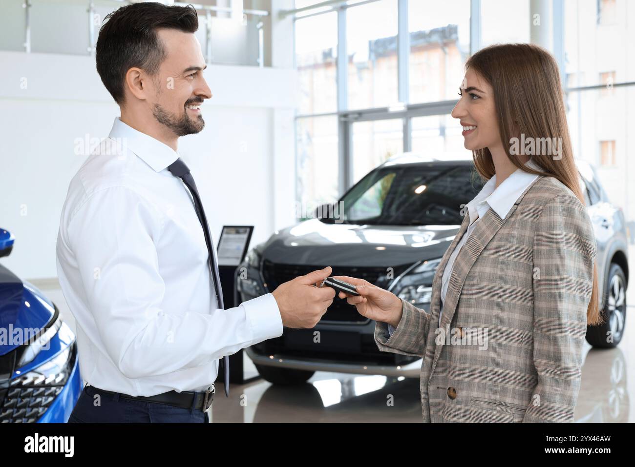 Saleswoman giving key to client near new car in salon Stock Photo - Alamy