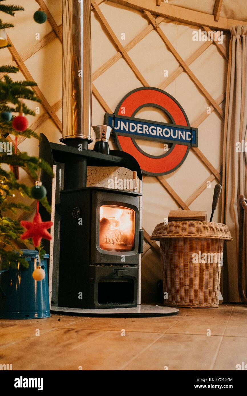 A wood burning stove is in front of a Christmas tree. A sign that says Underground is hanging on the wall Stock Photo