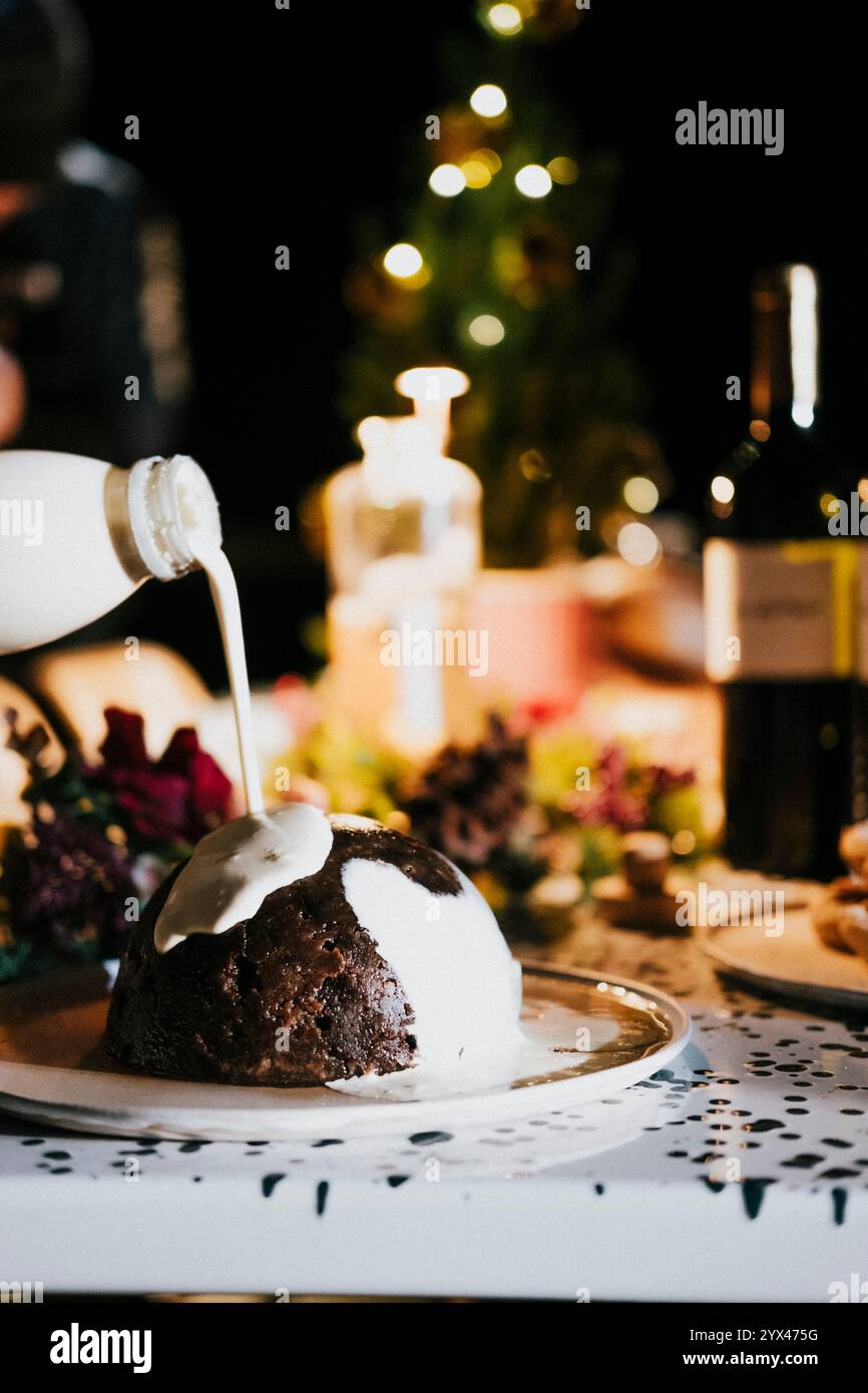 A white and brown dessert is being poured over a plate. The dessert is a type of cake, and the milk is being poured over it. The scene is set in a din Stock Photo