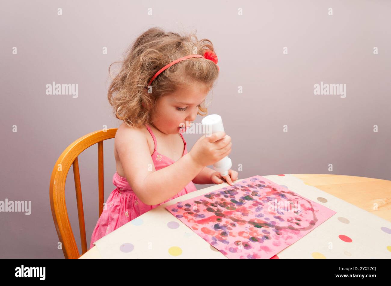 Three year old girl enjoying a creative activity painting a dot picture with a paint bottle. Stock Photo