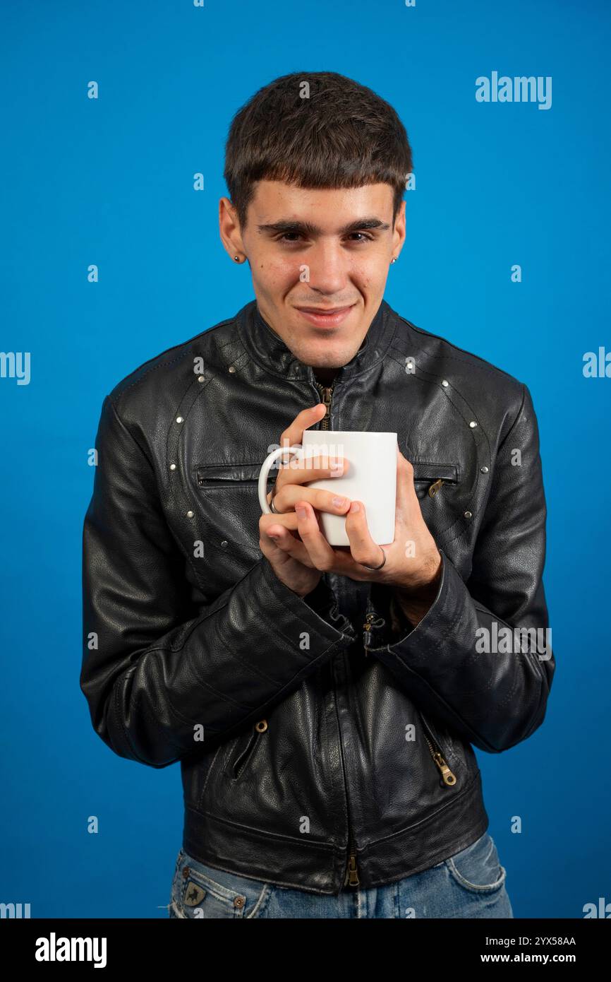 Stylish man enjoying a warm beverage in a white mug, against a vibrant blue backdrop Stock Photo