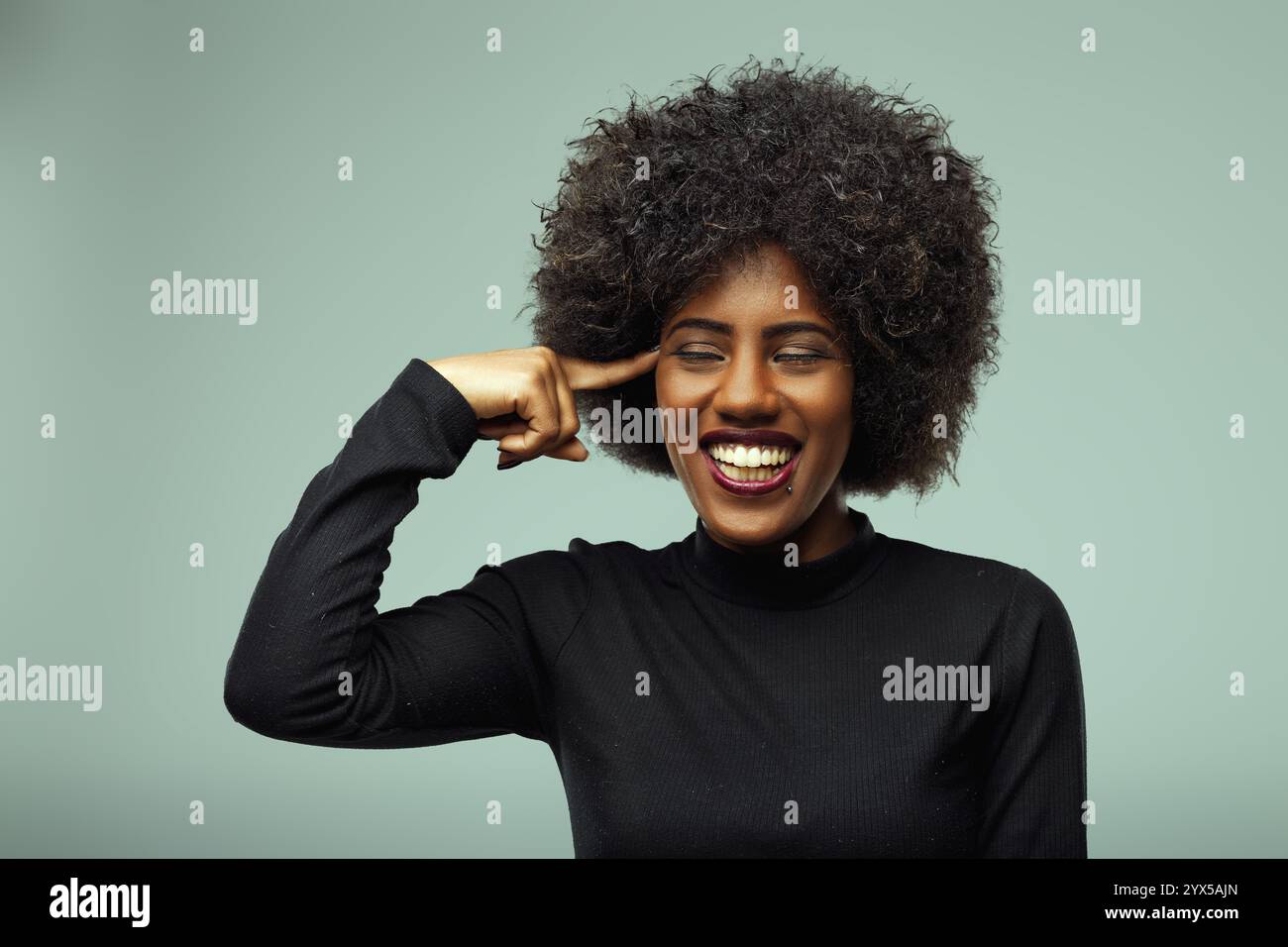 Studio portrait of a cheerful young woman with afro hairstyle pointing ...