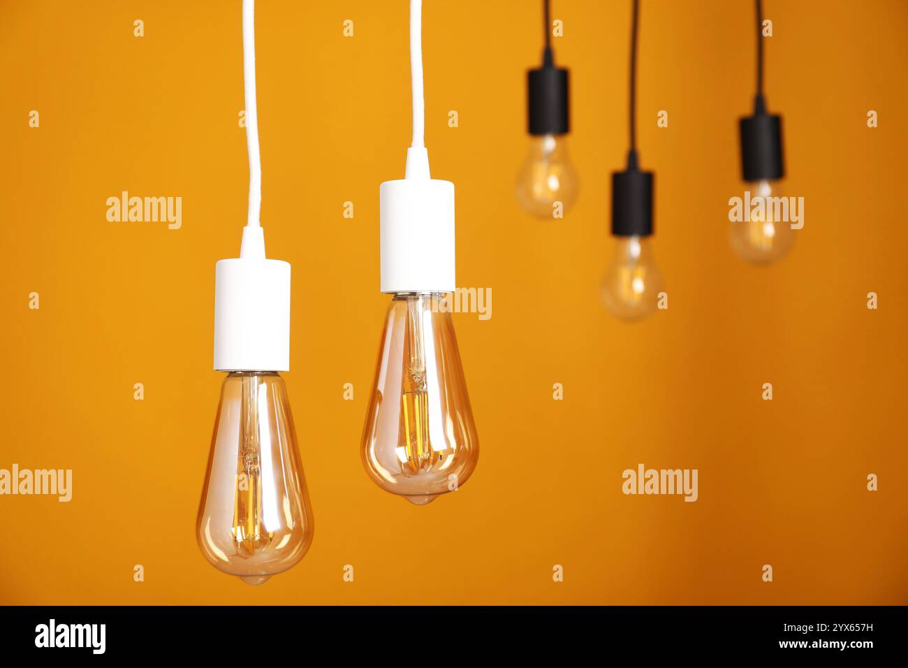 Light bulbs hanging on cords against orange background Stock Photo