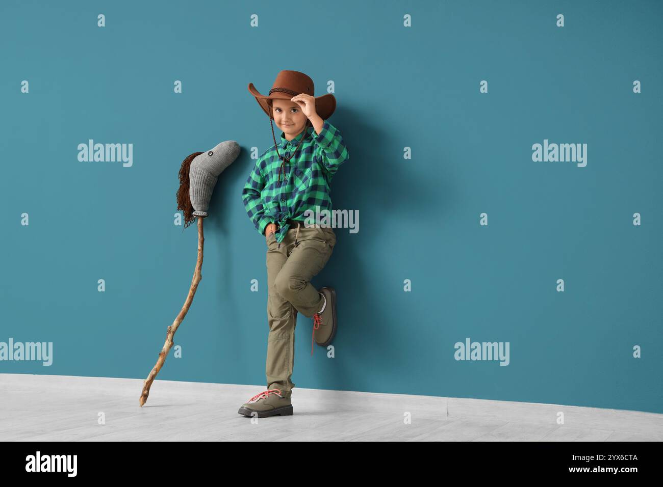 Cute little cowboy with toy horse near blue wall Stock Photo