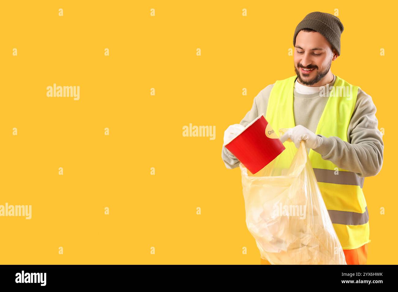 Male scavenger throwing food container into garbage bag on yellow ...