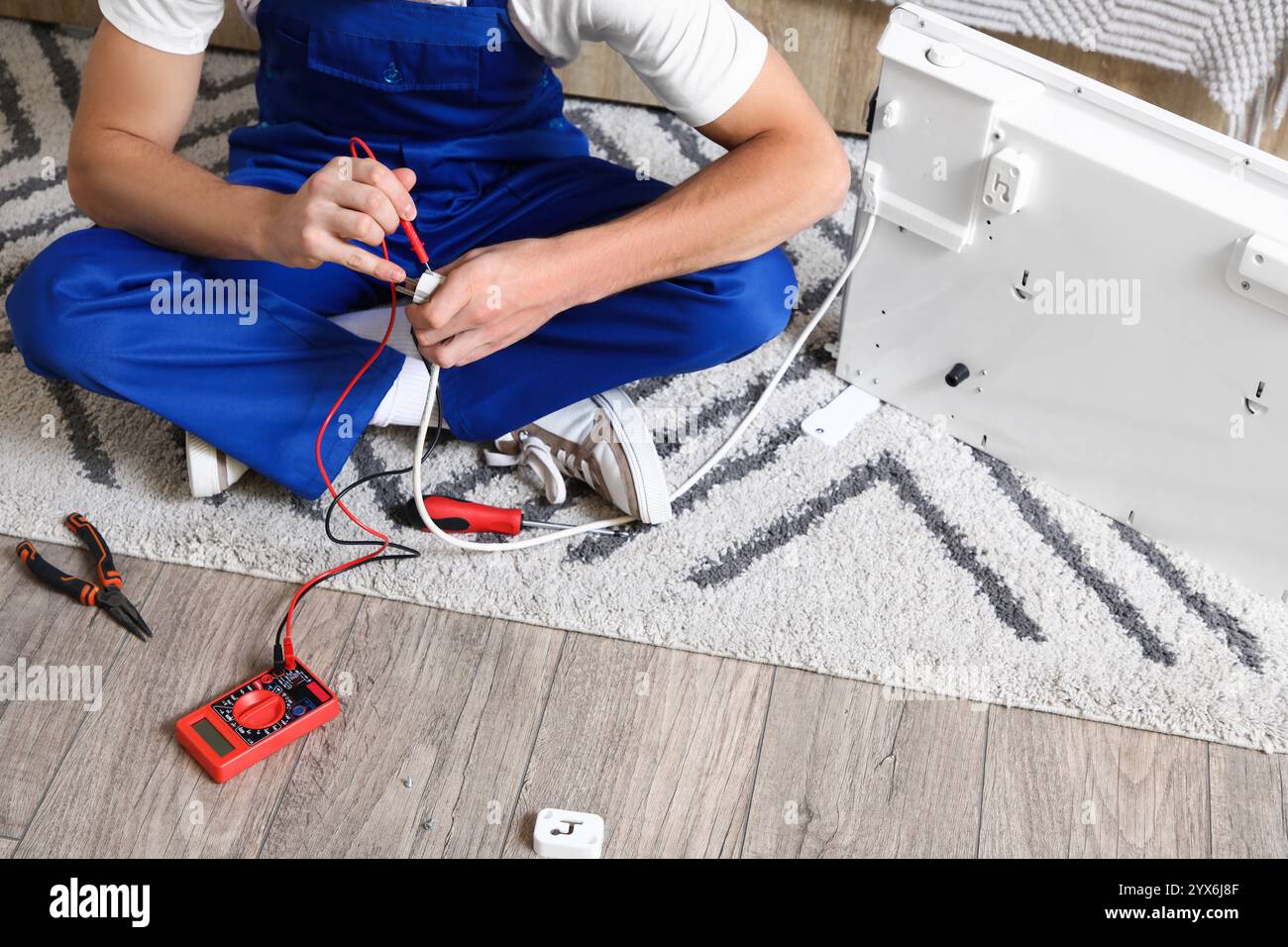 Male technician measuring voltage of electric convector heater in ...