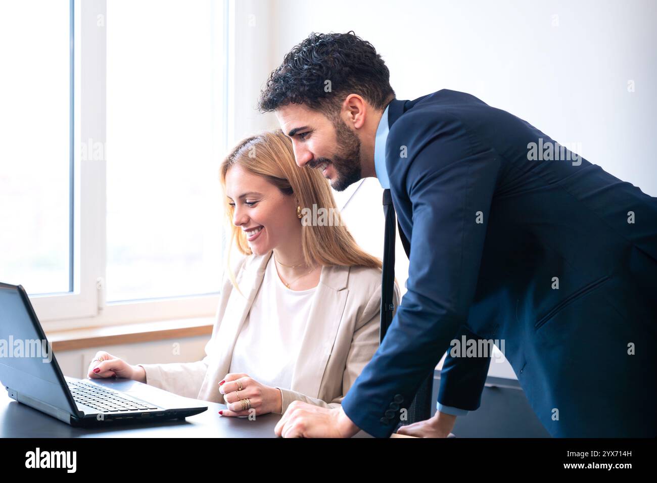 Colleagues Collaborating on Laptop in Bright Office Setting Stock Photo