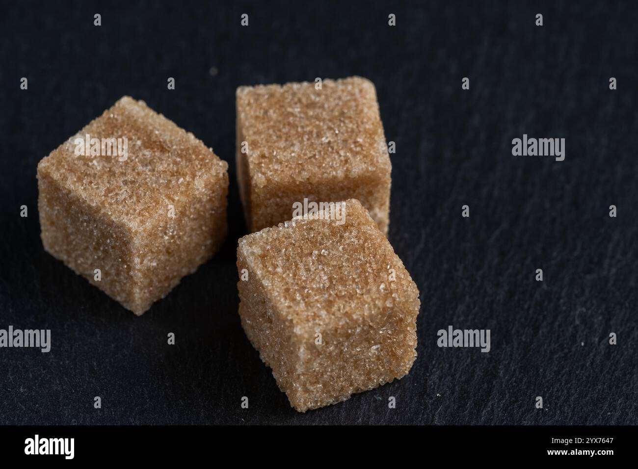 Brown cane sugar cubes on dark stone background, closeup Stock Photo