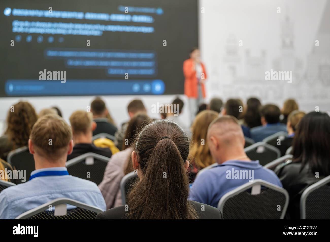 People gathered in a conference hall attending a business seminar with a speaker on stage. Stock Photo
