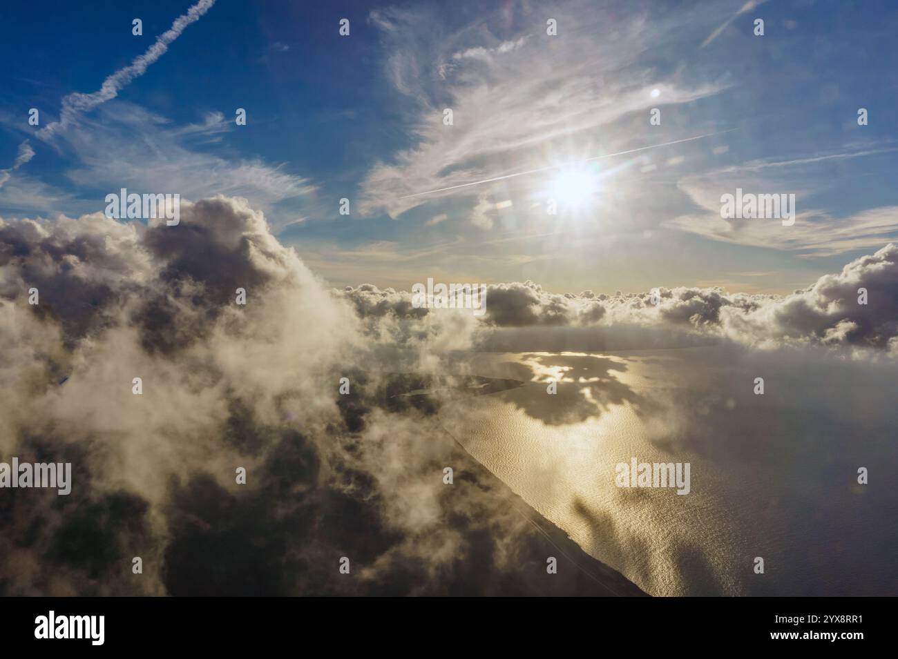 A plane is flying through a cloudy sky with the sun shining through the ...