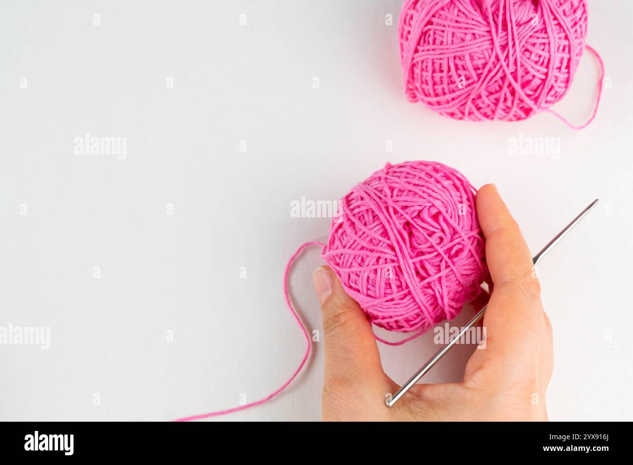Hand holding ball of pink yarn and a chrocket hook on light background, top view Stock Photo