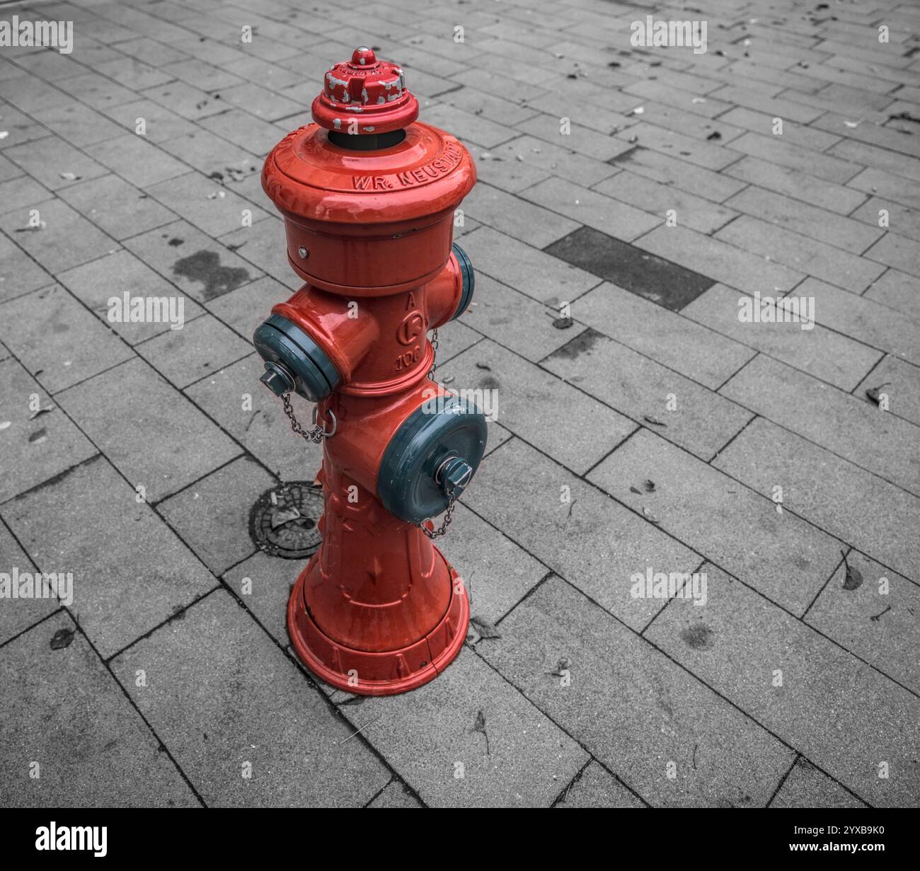A bright red fire hydrant stands on a clean, paved sidewalk with a gray tiled pattern in an urban environment. Stock Photo