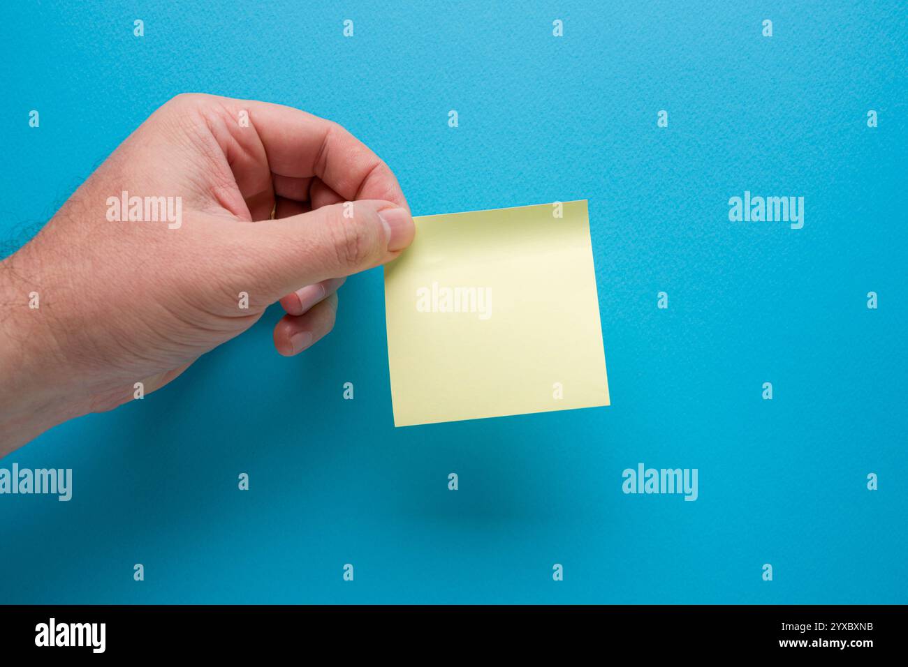 Hand holding blank yellow sticky note on blue background Stock Photo