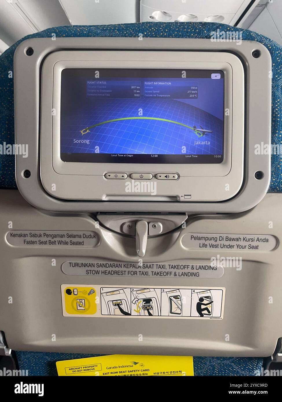 In-flight screen shows flight path Sorong-Jakarta. Seatback displays safety instructions, life vest location, and emergency exit operation steps - Smartphone Captured Stock Image