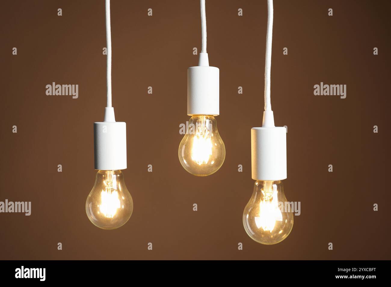 Light bulbs hanging on cords against brown background Stock Photo