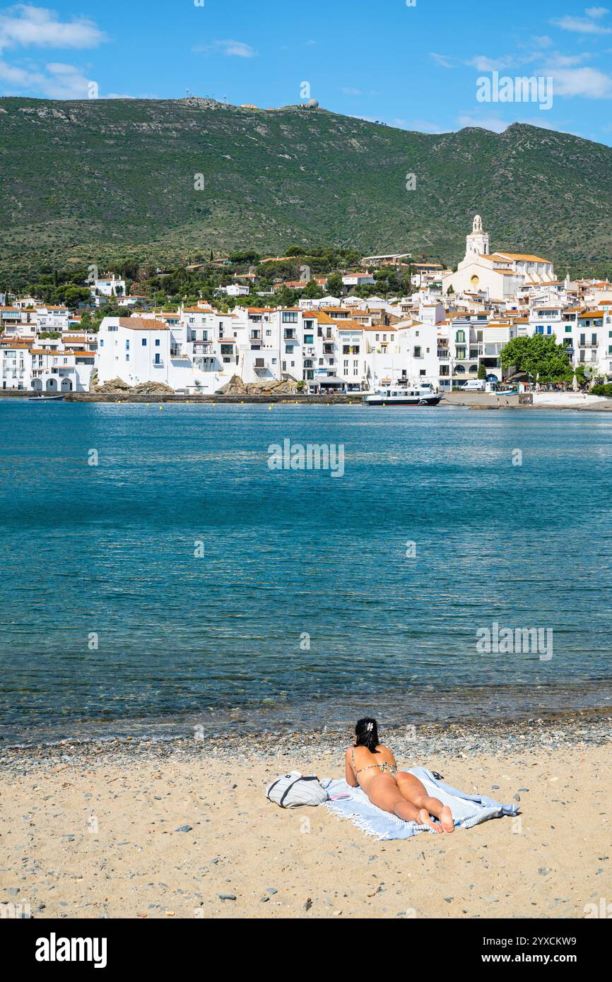 Young woman in a bikini lying on a sandy beach on the shore of the old town of Cadaqués in the sun, Catalonia, Spain Stock Photo