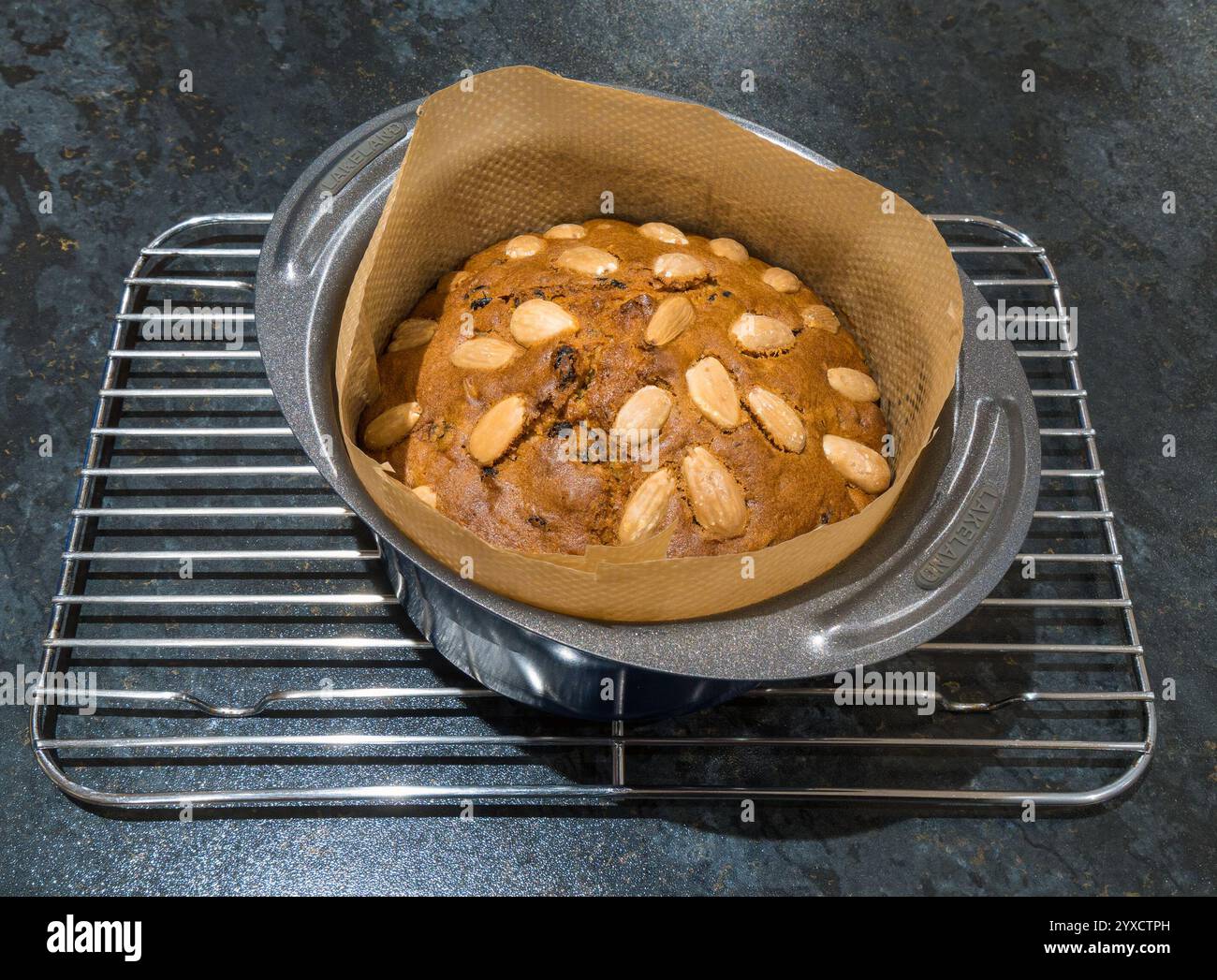 Small, round, freshly baked Dundee Cake topped with Almonds, still in lined baking tin on cooling rack. Stock Photo