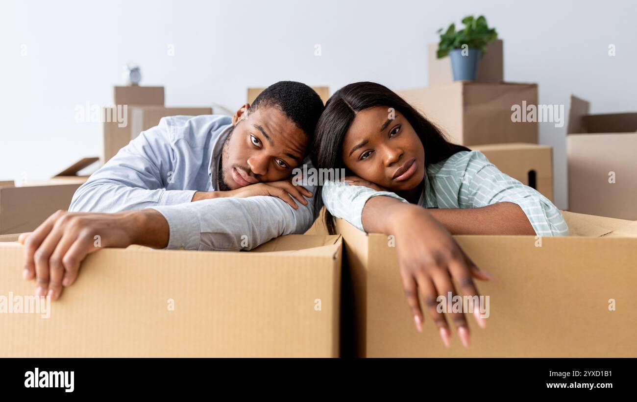 Moving stress concept. Exhausted black family leaning on unpacked boxes ...