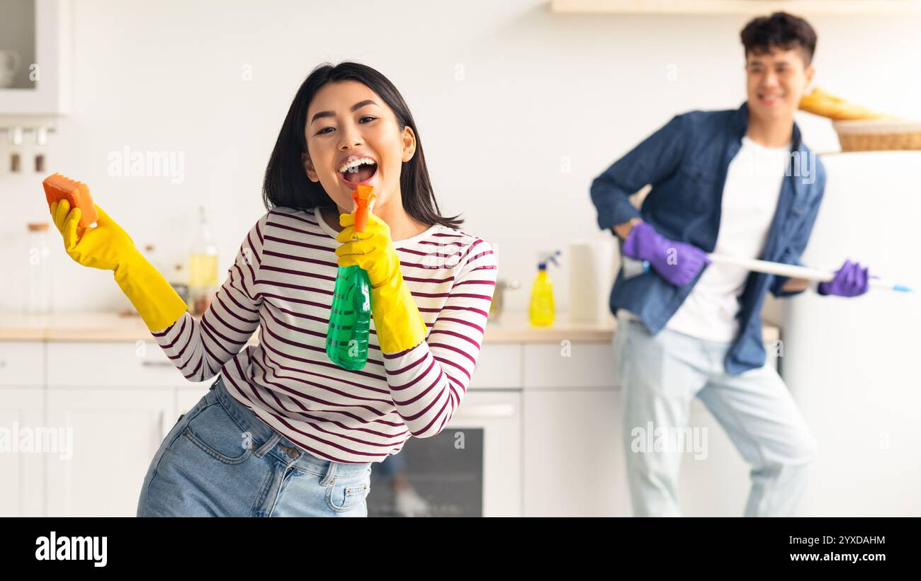 Joyful asian lady using spray as microphone, singing while cleaning Stock Photo