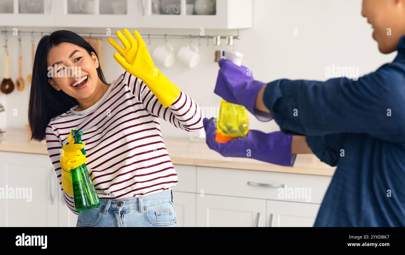 Playful asian lovers having fun while cleaning house together Stock Photo