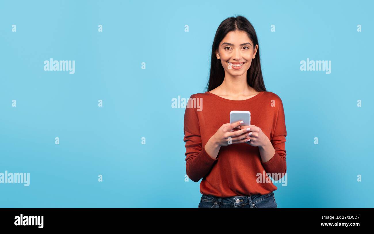 Woman smiling while using smartphone against bright blue background Stock Photo