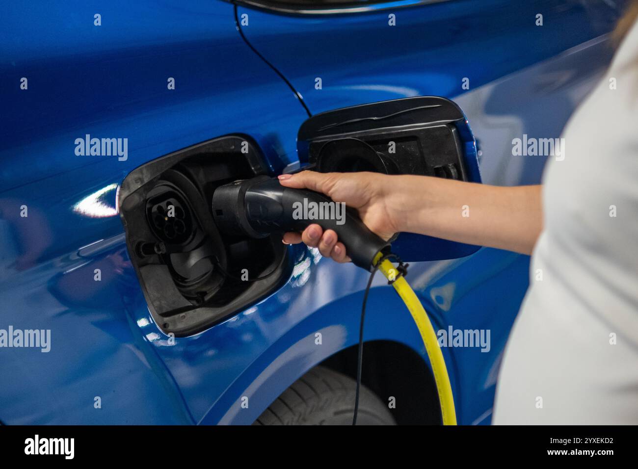 Woman connects a charging cable to an electric car in a public parking area Stock Photo