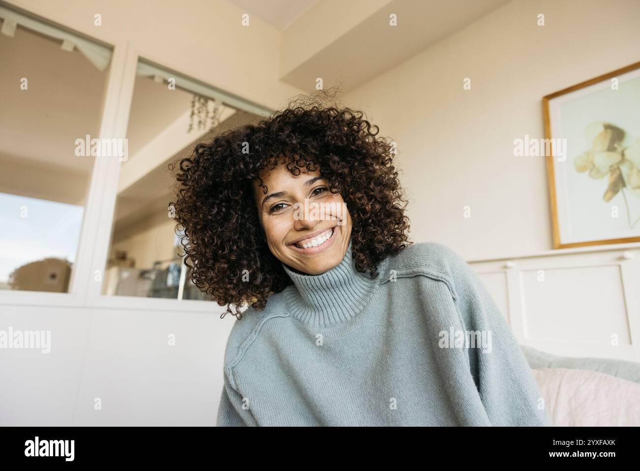 A cheerful woman with curly hair smiling warmly while sitting ...