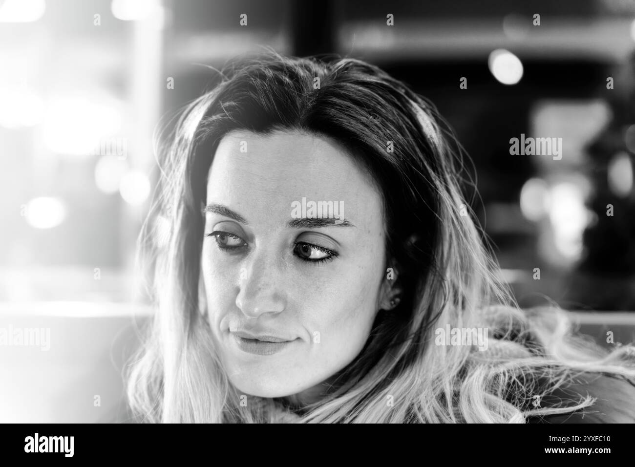 Black and white close-up portrait of a young woman looking sideways in soft light, conveying emotion, contemplation, and inner thoughts. Stock Photo