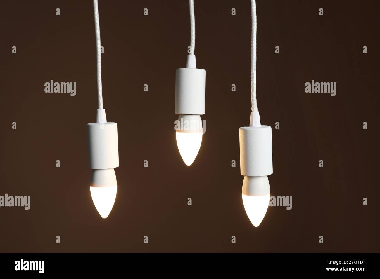 Light bulbs hanging on cords against brown background Stock Photo