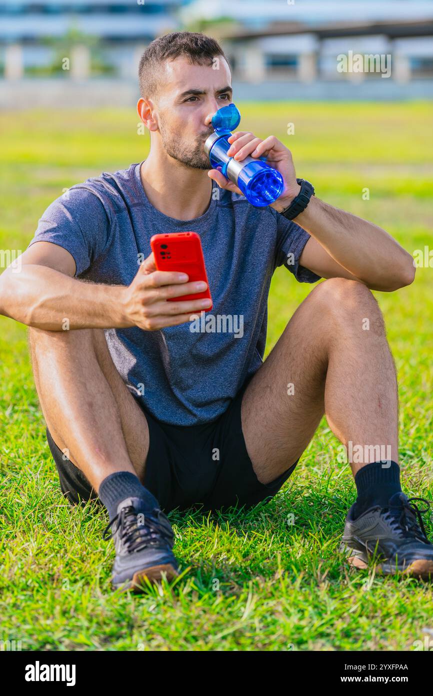 Picture of Athletic man sitting on grass drinking water and holding.Vertical Stock ...
